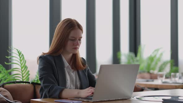 A Young Redhaired Woman is Working on a Laptop alt