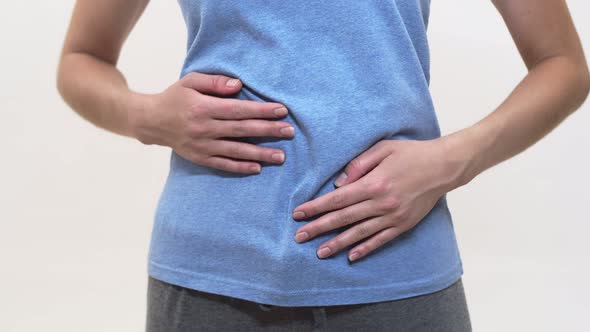 Woman in Blue Tshirt Grabs Sick Stomach on White Background Closeup alt