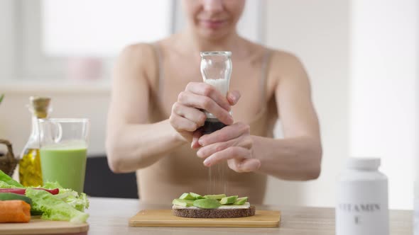 Blurred Woman Salting Sandwich with Cucumber and Rye Bread Sitting at Table Indoors alt