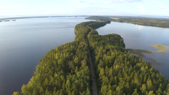 Aerial shot of following a car driving on road that goes through island surrounded by a lake in Finl alt