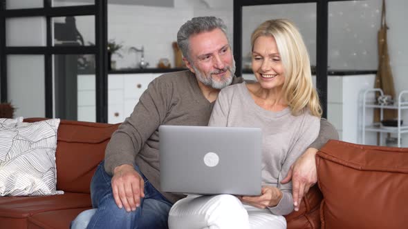 Carefree Middleaged Spouses Using Laptop Sitting on the Sofa in Modern Living Room alt