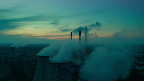 A bird's eye view of the plant, at sunset, large pipes of the plant release steam