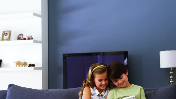 Siblings using digital tablet in living room alt