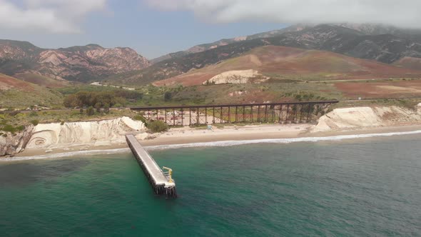 Drone flies around pier revealing train track along the coastline