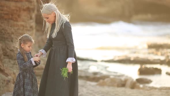 Young Mother and Daughter Play and Walk on the Stone Beach in the Sunset Slow Motion