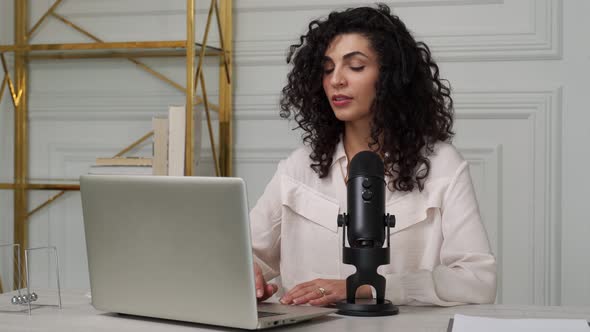 Curlyhaired Brunette Woman with a Microphone and Laptop Talking and Recording a Podcast in the alt