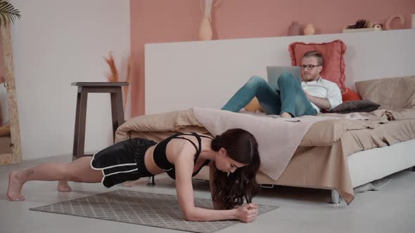 Couple at Home Doing Different Activities Woman Exercising and Man Working Freelancing at Laptop