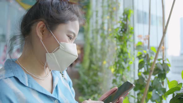 attractive asian female casual cloth wearing facial face mask virus protecting hand use smarthpone alt