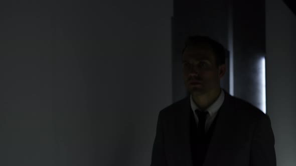 Man in a Suit Walks Along a Dark Corridor Near Doors of an Illuminated Apartment