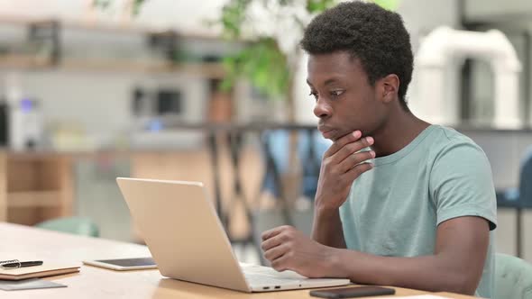 Pensive Young African Man Thinking and Working on Laptop alt