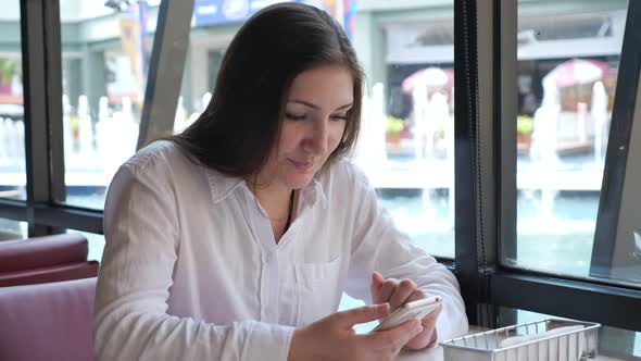 Brunette Woman with a Phone at a Table in a Cafe alt