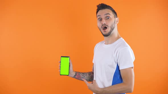 Soccer Fan In White Blue Shirt Show Green Screen Smartphone Orange Background  alt