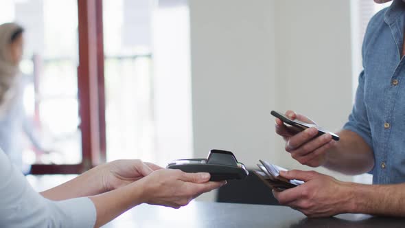 Caucasian man talking and paying with smartphone at reception at modern dental clinic alt