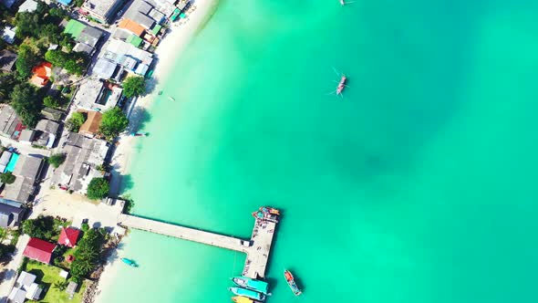 Sandy beach and pier over the turquoise seawater. Boats floating in the calm lagoon with luxury reso alt