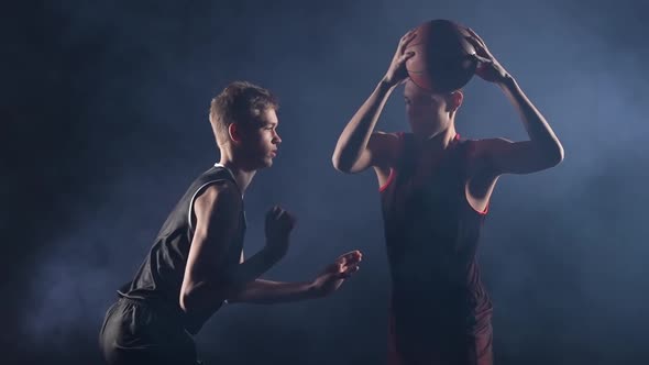 Two Young Athletes Practice Basketball in a Dark Smoky Studio Under the Spotlight alt