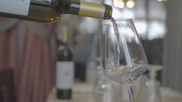 Close-up of unknown waiter hand pours white wine into glass in restaurant interior indoors. 4k