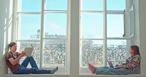 a Man and a Woman are Sitting on the Window and Reading alt