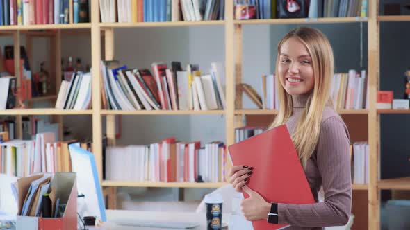 Long-haired Blonde Holds Red Folder , Smiling with White Teeth