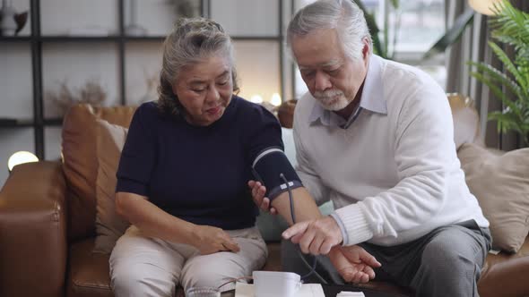 Asian elderly couple using a blood pressure monitor to the wife in the house alt