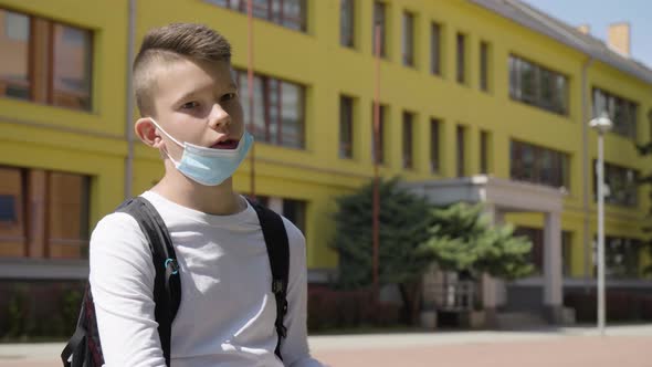 A Caucasian Teenage Boy in a Face Mask Talks to the Camera  a School in the Background