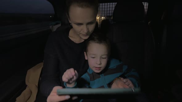 Mother and son playing with touch pad during night car ride alt