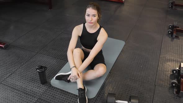 Young Athletic Woman Sitting on a Mat in the Gym Getting Ready for Sports