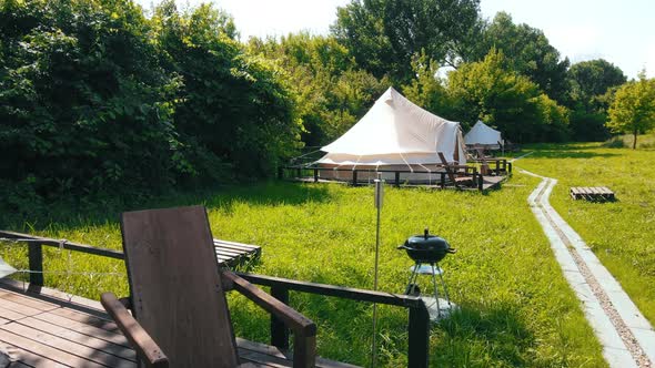 Glamping tents with chairs in the nature, green grass and trees, trail alt