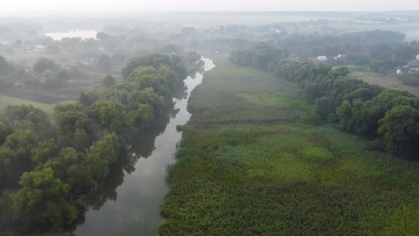 Foggy Morning Over a Plain and River Floodplain Meadow Near a Rural Village with a House alt
