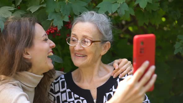 Adult Daughter and Senior Mum are Taking Selfportrait Picture Selfie on Red Smartphone Together alt