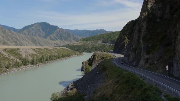 Traffic cars on Chuya highway road between mountains and Katun river under blue sky in Altai
