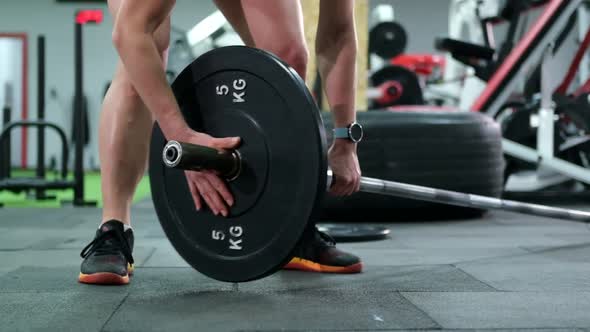 Close-up on the hands: The bodybuilder gives extra weight to the barbell. alt