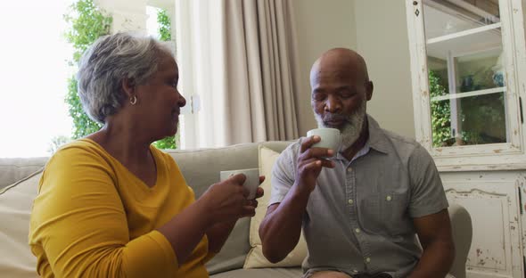 African american senior couple smiling while having coffee together sitting on the couch at home alt