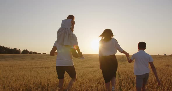 A Young Family With Children Run Across The Field, Holding Hands