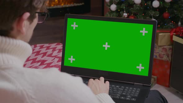 Over the Shoulder: Man Using Laptop with Mock-up Green Screen. alt