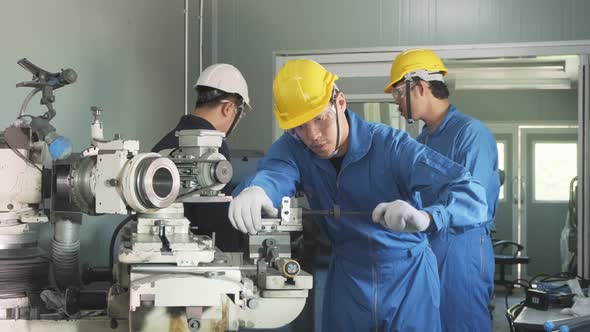 Asian mechanical technicians workers team wear helmet working on milling machine in industry factory alt