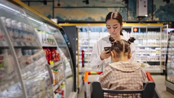 Young Mother Walks in Supermarket Looking at Shopping List alt