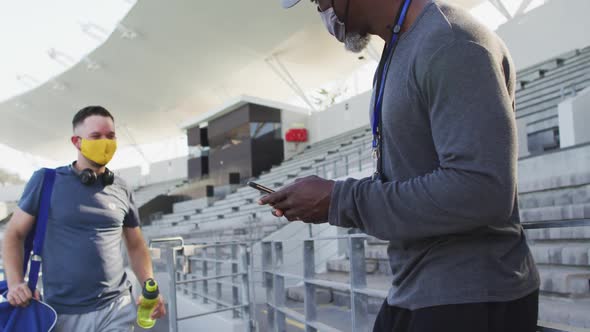 Diverse male coach and athlete wearing face mask touching elbows before training session alt