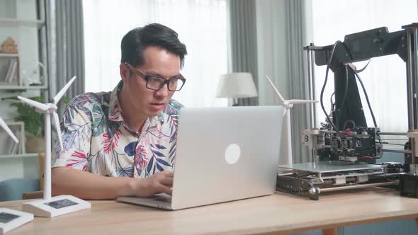 Asian Man With Laptop Computer Programming Electric Wind Turbine Model At Home alt