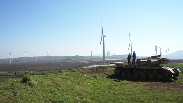 people walking on a tank with windmills in the background