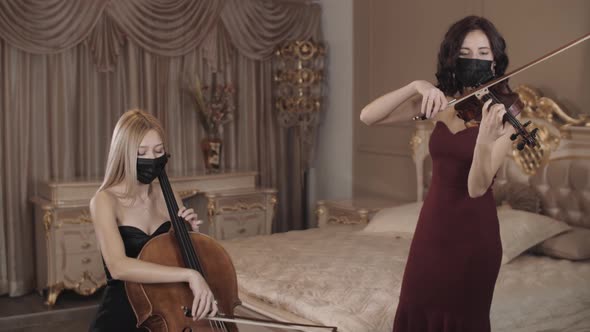 Symphonic duet. Two girls in beautiful dresses and masks play the violin and cello. violin and cello