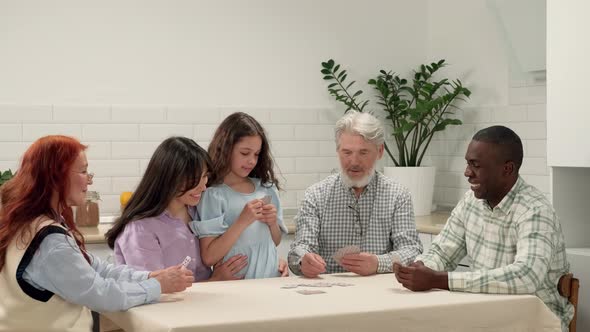 Cheerful Multiethnic Family of Different Age Generations Play Cards at Home Sitting at the Table alt