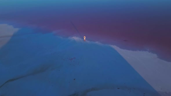 Drone Flying From Man Pilot Standing on Coast of Pink Lake at Sunset alt