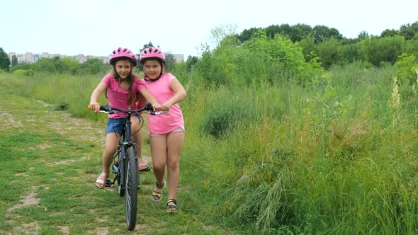 Two little girls in pink Bicycle helmets in nature. The older sister teaches the younger