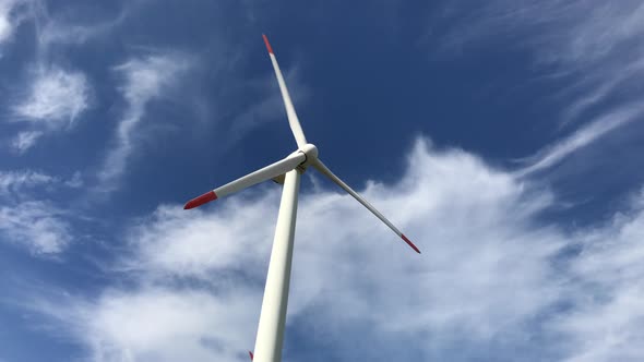 Closeup front back footage of a giant wind turbine with three blades with blue sky and clouds in the alt