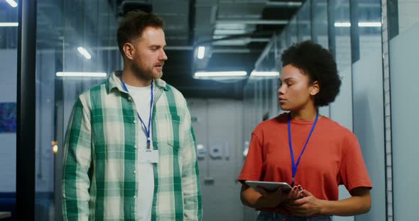 Young Colleagues Use a Tablet and Talk As They Walk Down the Office Center alt