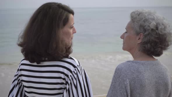 Mature Brunette Woman Narrating Something To Senior Woman on Seashore alt