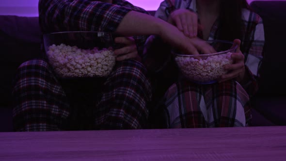 Married Couple in Pajamas Sitting in Front of the TV and Eating Popcorn alt