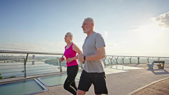 Cheerful Slim Pensioners Enjoy Running in City at Sunrise alt
