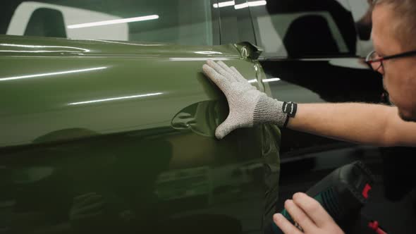 Man Smoothing the Vinyl Film on a Car Door in a Work Garage Wrapping a Car