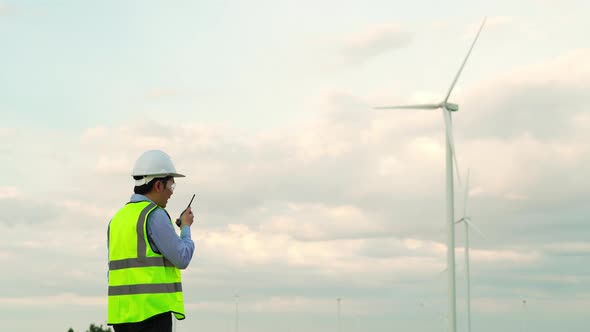 young male engineer using walkie talkie to checking system against wind turbine farm